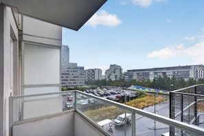 Vista desde un balcón sobre un estacionamiento con varios coches y un edificio al fondo.