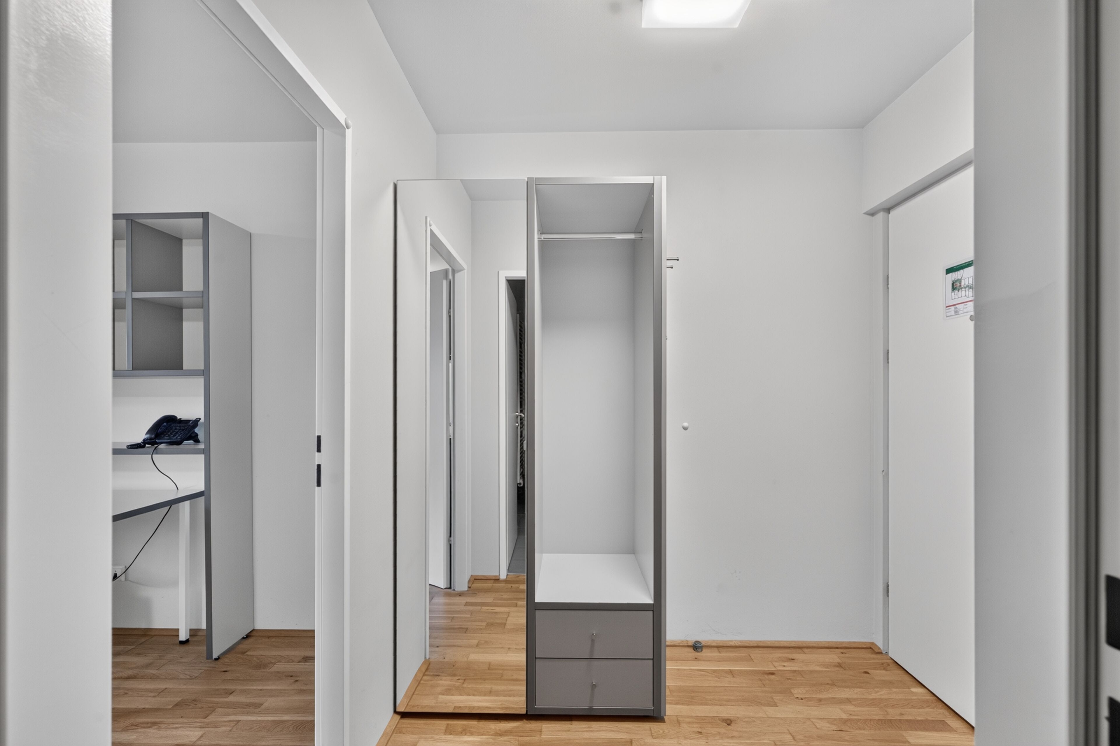 Un pasillo con un armario, un escritorio con teléfono y una puerta que da a otra habitación.
