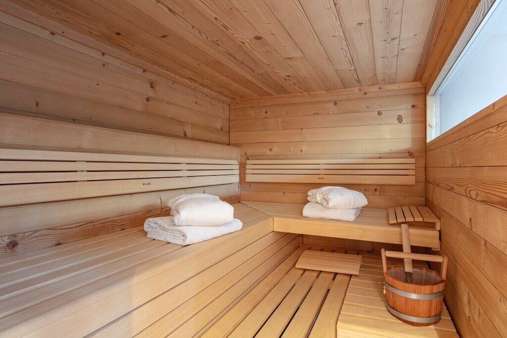 A sauna room with wooden benches, towels, and a wooden bucket.