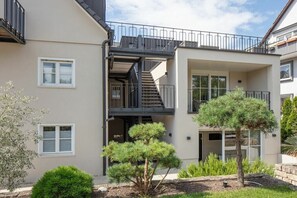 Een meerlaags woongebouw met een balkon, een trap en een klein tuinpartij met bomen.