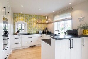 Une cuisine moderne avec des meubles blancs, un plan de travail noir et un pare-feu décoré de motifs.
