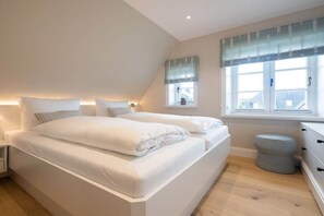 Une chambre à coucher avec un grand lit, une table de chevet, une fenêtre avec des rideaux et un petit tabouret.