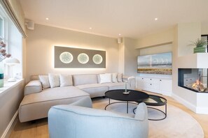 Un salon moderne avec un canapé d’angle, une table basse ronde et une cheminée.