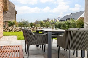 Un patio al aire libre con una mesa y sillas, un muro de piedra y una zona verde.