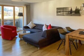 Ein modernes Wohnzimmer mit einer Couch, einem roten Sessel und einem Esstisch.