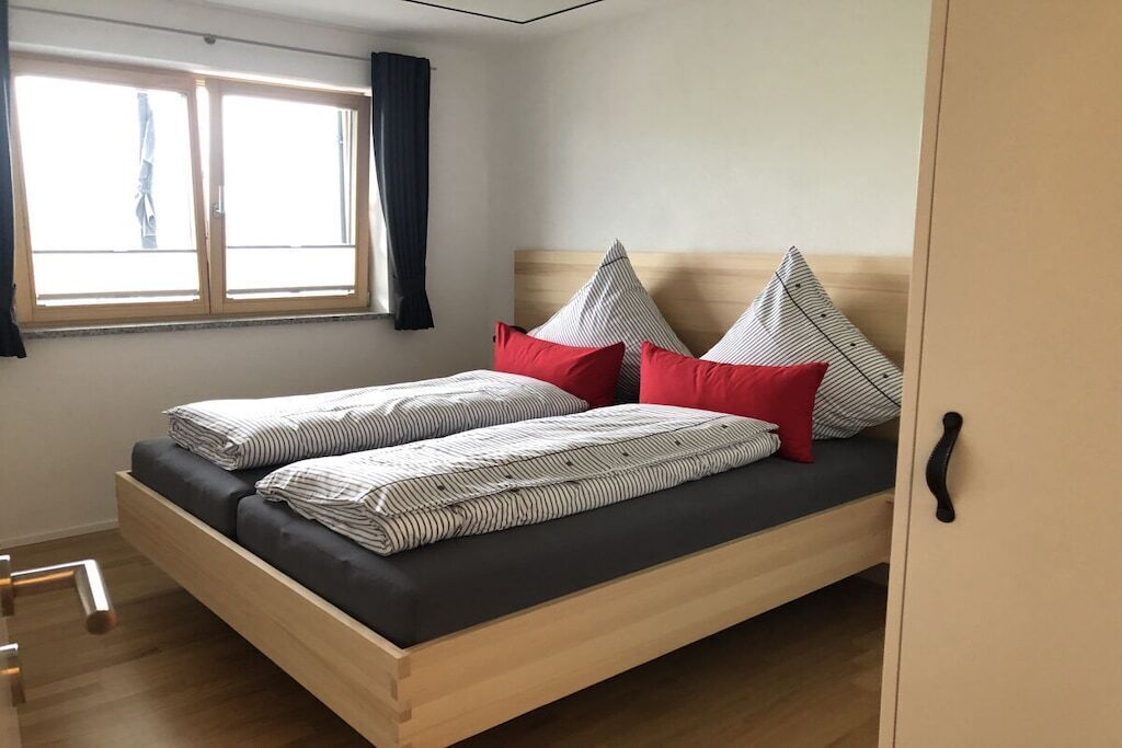 Un letto singolo con struttura in legno, materasso nero e cuscini a righe.