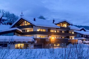 A multi-story building with a snow-covered roof and multiple illuminated windows. - Holiday apartment with 2 bedrooms (Oberstdorf)