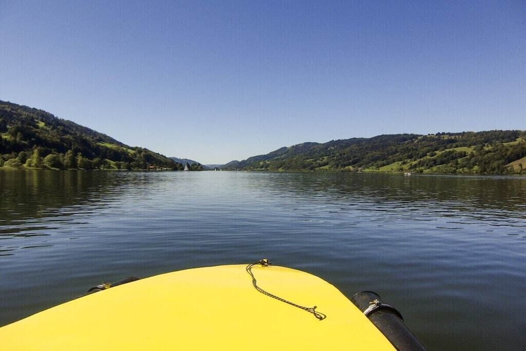 Une rivière paisible, avec un objet jaune au premier plan, le tout entouré d’un paysage vallonné.