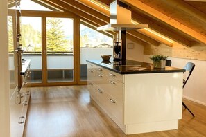 A modern kitchen with a central island, wooden ceiling beams, and a view of the outdoors. - Holiday apartment with 2 bedrooms (Oberstdorf)