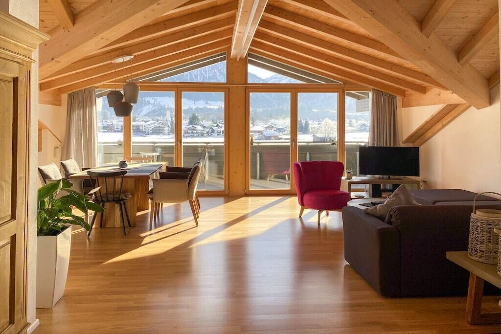 Een ruime woonkamer met een houten plafond, een eettafel met stoelen, een rode fauteuil, een bank en een televisie.