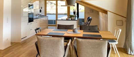 A modern kitchen with wooden beams, a dining area with a wooden table and chairs, and a view of the outdoors.