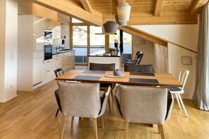 A modern kitchen with wooden beams, a dining area with a wooden table and chairs, and a view of the outdoors. - Holiday apartment with 2 bedrooms (Oberstdorf)
