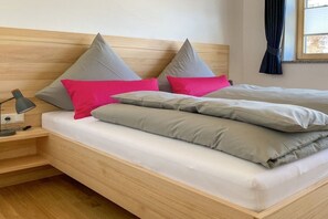 A bed with grey and pink pillows, a bedside lamp, and a wooden headboard. - Holiday apartment with 2 bedrooms (Oberstdorf)
