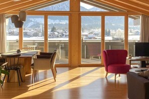 A spacious living area with a large sliding glass door leading to a balcony, wooden flooring, and a red armchair. - Holiday apartment with 2 bedrooms (Oberstdorf)