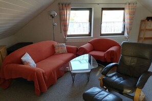 Ein gemütliches Wohnzimmer mit einem roten Sofa, einem Glastisch und einem schwarzen Ledersessel.