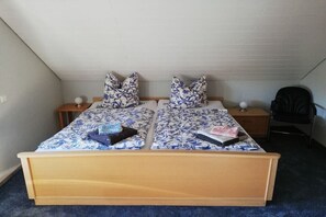 A double bed with a floral bedspread, two pillows, a nightstand, a chair, and a desk with a lamp. - Stender "An der olen Au" (Winsen)