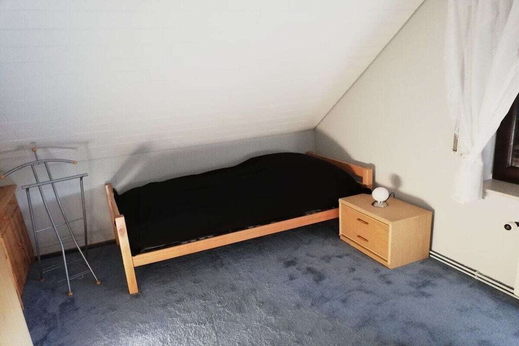 Ein kleines Zimmer mit einem Einzelbett, geneigter Decke, einem Holz-Nachttisch, einer Lampe und einer Heizung.