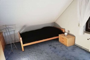 Une petite chambre avec un lit simple, un plafond en pente, une table de chevet en bois, une lampe et un radiateur.