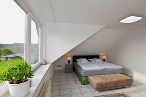 Ein Schlafzimmer mit Bett, Nachttischlampen, einer Topfpflanze und Blick auf eine grüne Landschaft.
