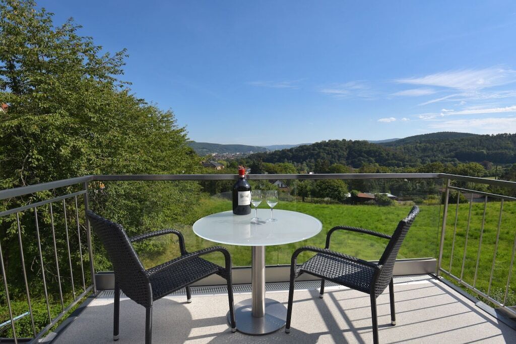 Un balcón con una mesa redonda y dos sillas, con vistas a un paisaje verde con colinas.