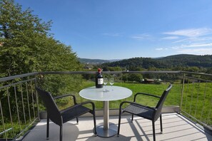Ein Balkon mit einem runden Tisch und zwei Stühlen, der auf eine grüne Landschaft mit Hügeln blickt.