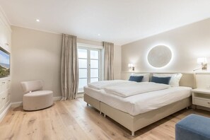 Un dormitorio con una cama grande, una mesita de noche, una silla y una ventana con cortinas.