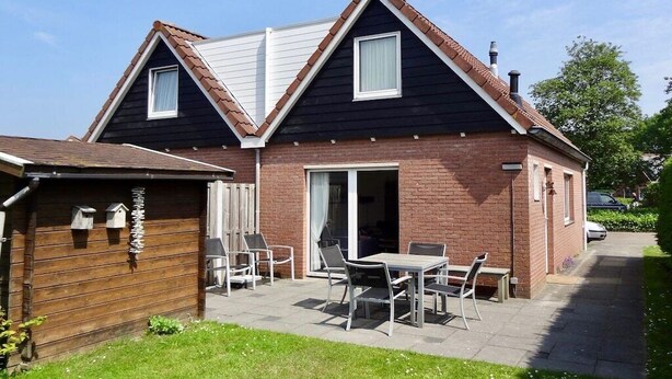 Une maison à deux étages avec un patio, une clôture en bois et une voiture garée dans l’allée.