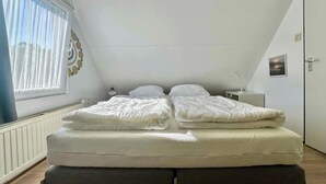 Une chambre à coucher avec un lit, une table de chevet, une fenêtre avec des rideaux et un élément décoratif mural.
