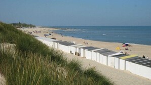 Une plage bordée d’une rangée de cabanes de plage blanches, avec du sable fin et la mer.