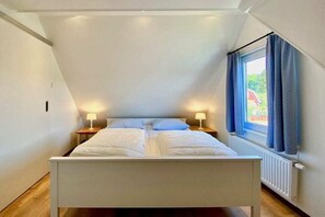 Ein Schlafzimmer mit einem Bett, zwei Nachttischen mit Lampen, einem Fenster mit Vorhängen und einer Heizung.