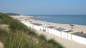 Une plage bordée d’une rangée de bâtiments blancs, une étendue de sable et l’océan.