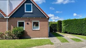 Une maison à deux étages, avec une façade en briques, un toit recouvert de tuiles rouges et une pelouse bien entretenue.