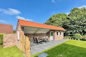 Ein Ziegelhaus mit überdachter Terrasse, Rasenfläche und Holzzaun.