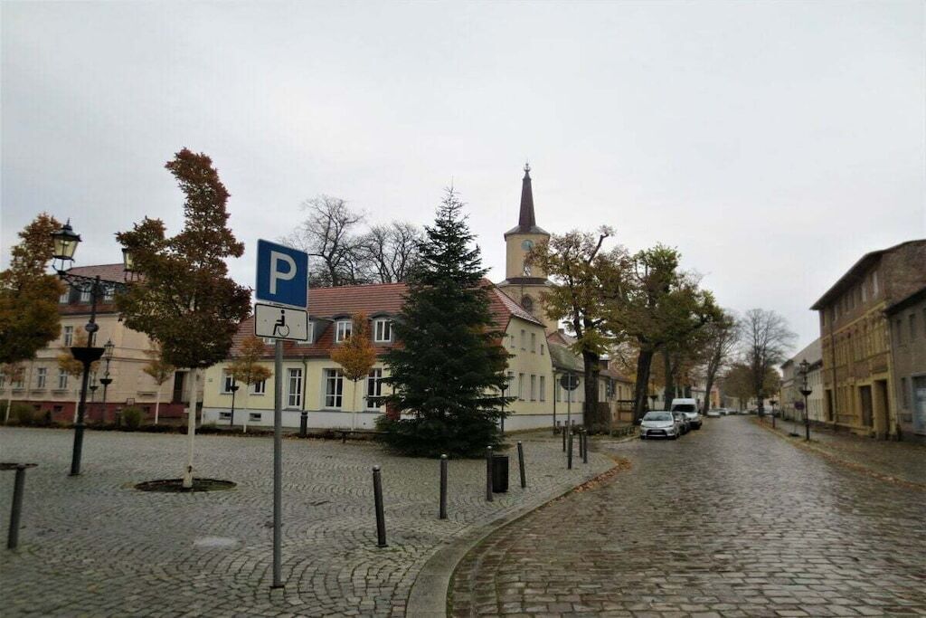Una calle adoquinada con una aguja de iglesia, un árbol de Navidad y una señal de estacionamiento.