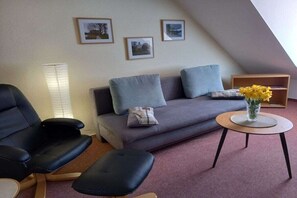 Una sala moderna con un sofá gris, sillones negros, una pequeña mesa redonda con un florero y cuadros en la pared.