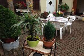 Un patio con mesa y sillas, plantas en macetas y suelo de ladrillo.