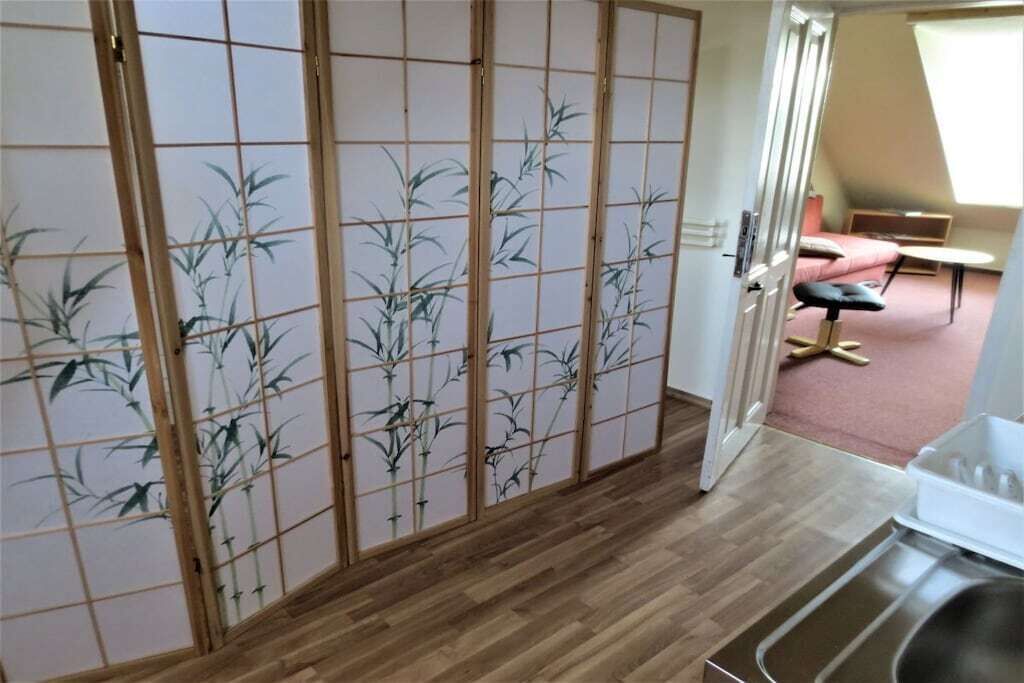 Ett rum med en skjutbar shoji-skärm, ett trägolv, ett litet bord och en bänk.