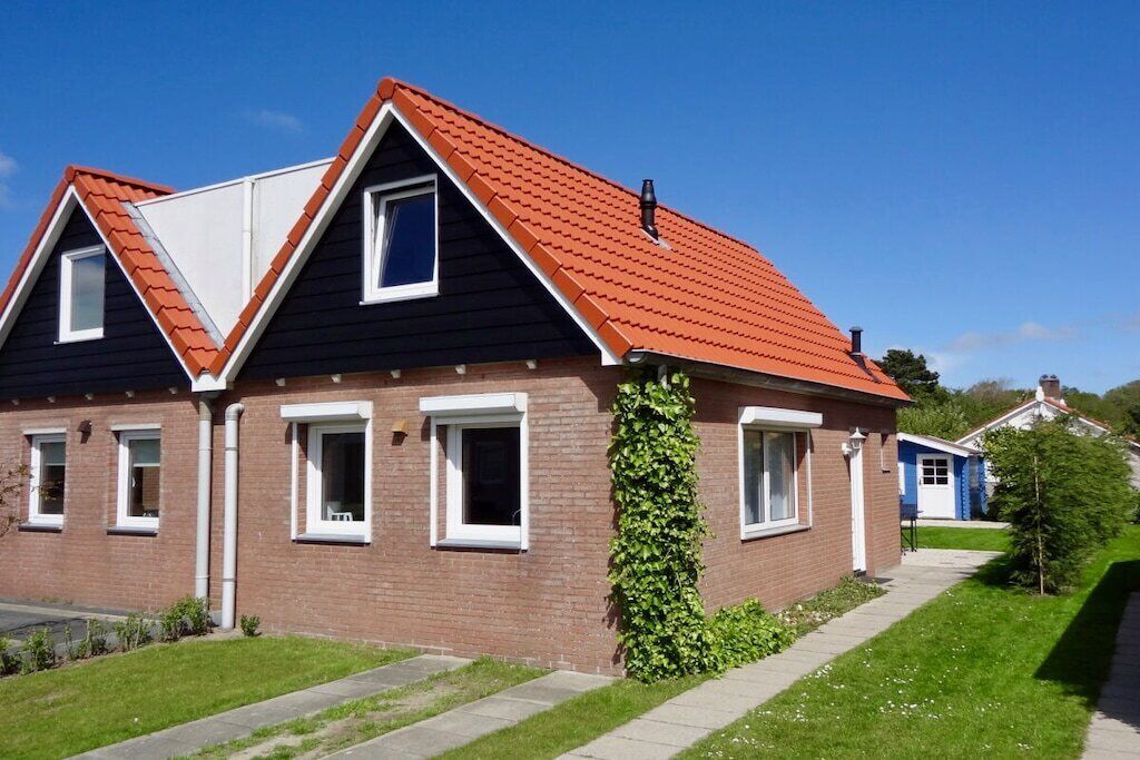 A two-story house with a red roof, brick exterior, and a small garden area.