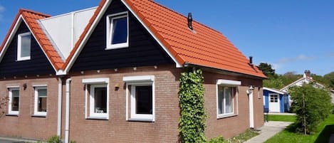 A two-story house with a red roof, brick exterior, and a small garden area.