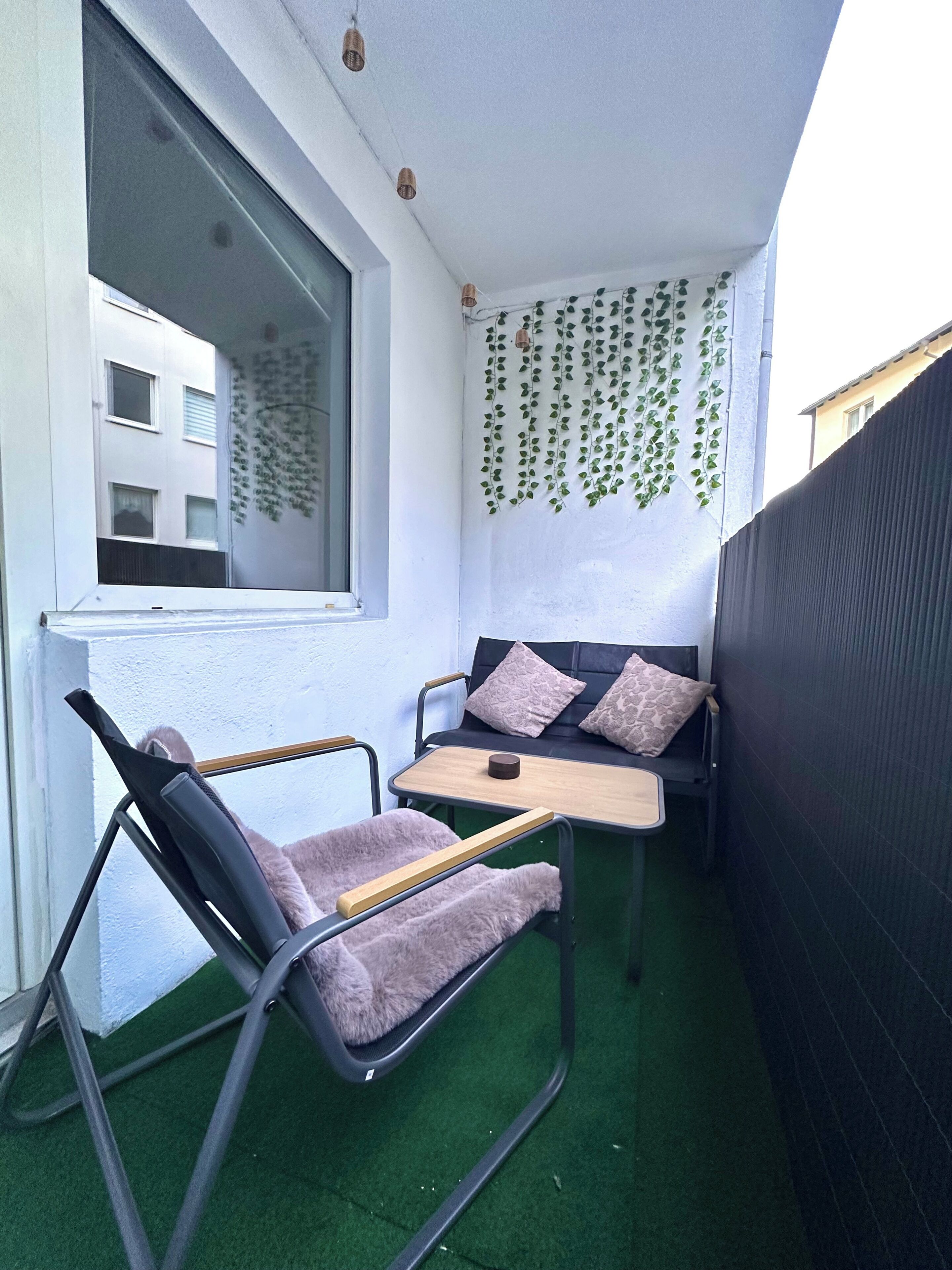 Ein kleiner Balkon mit einem schwarzen Stuhl, einem Holztisch und einer Couch mit Kissen.