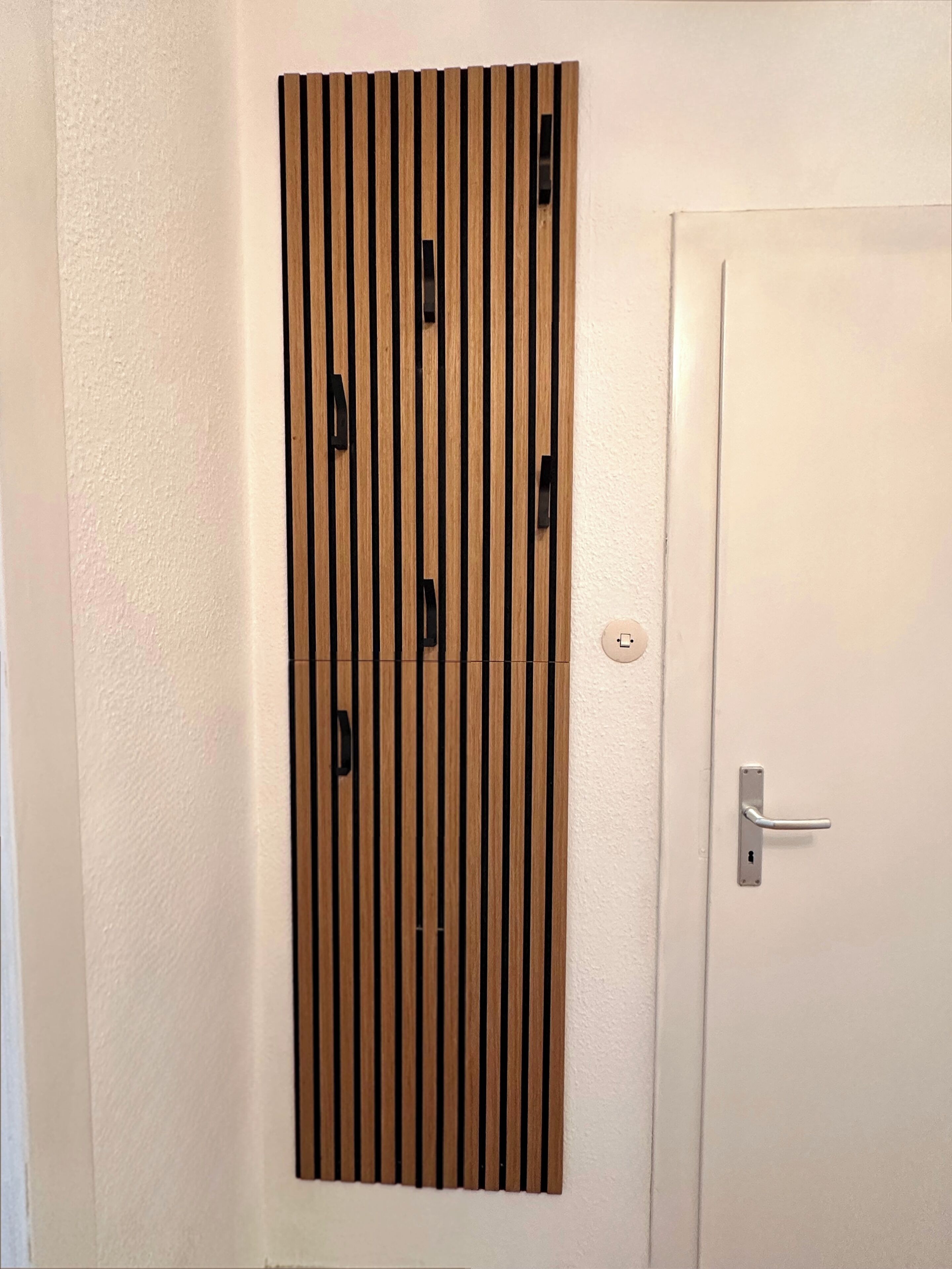 Eine weiße Tür mit silberner Klinke und einem vertikalen Holzpaneel mit schwarzen Griffen.