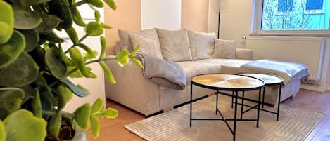 A living room with a sofa, a coffee table, a potted plant, and a window with a view.