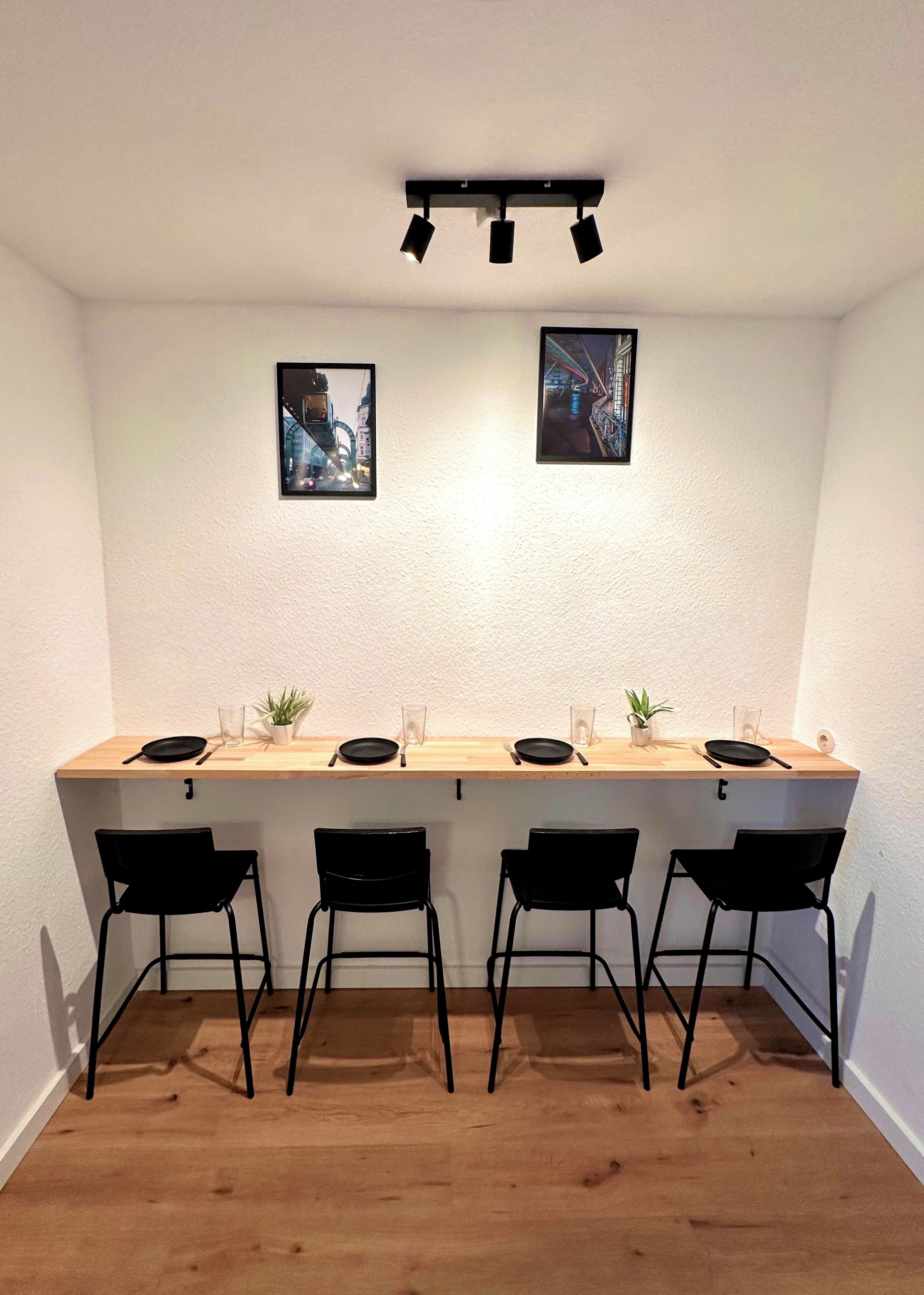 Ein Essbereich mit einem Holztisch, vier schwarzen Stühlen und zwei an der Wand hängenden Bildern.