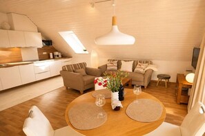 Un intérieur moderne comprenant un coin repas, des canapés, une cuisine et une grande fenêtre.