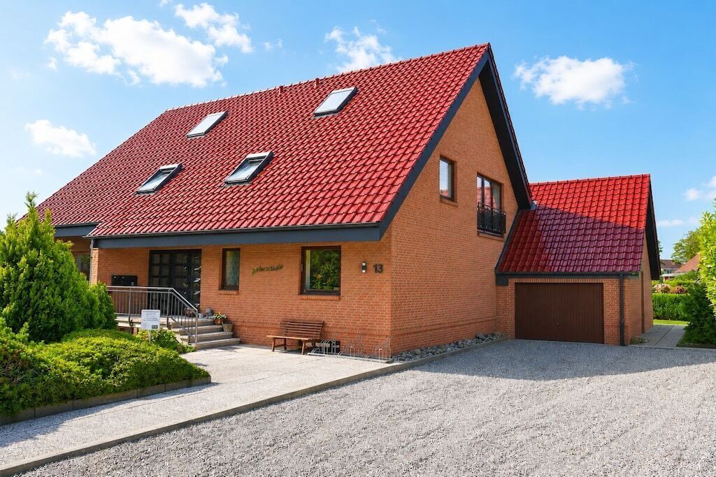 Een tweelaags huis met een rode dakbedekking van tegels, een gevel van baksteen en een oprit van grind.