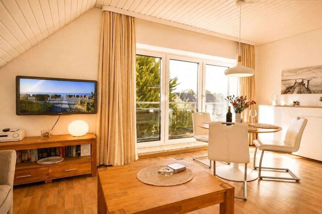 A modern living room with a television, a wooden coffee table, and a dining area with chairs.