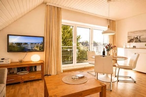 A modern living room with a television, a wooden coffee table, and a dining area with chairs. - Holiday apartment with 1 bedroom (Kellenhusen)
