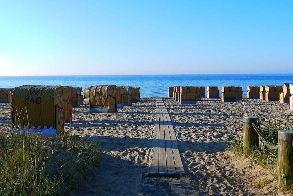 A wooden boardwalk leading to beach huts numbered 140, with the sea in the background.