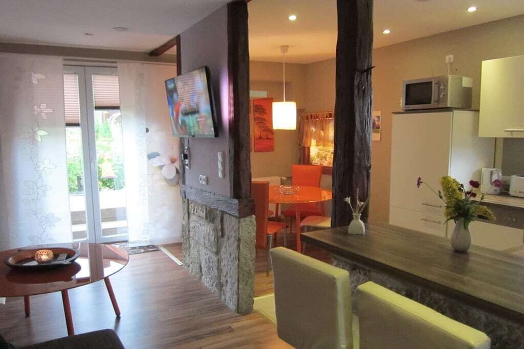 Une cuisine moderne équipée d’un four à micro-ondes, un coin repas avec une table et des chaises, et un salon avec un téléviseur et une cheminée.