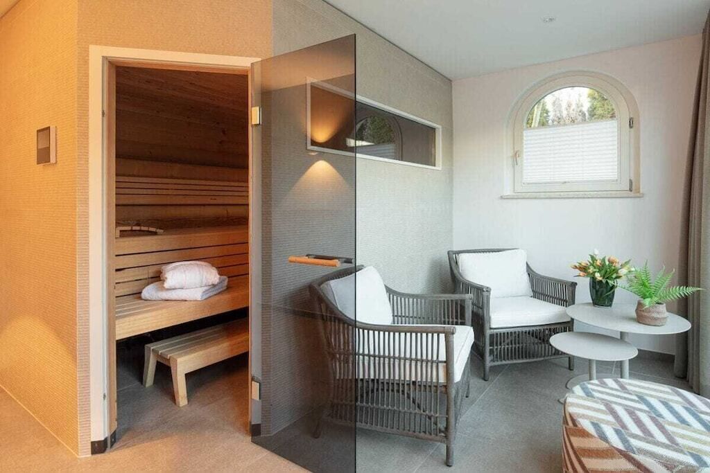 A modern room with a sauna, wicker chairs, a small table with a plant, and a window with blinds.